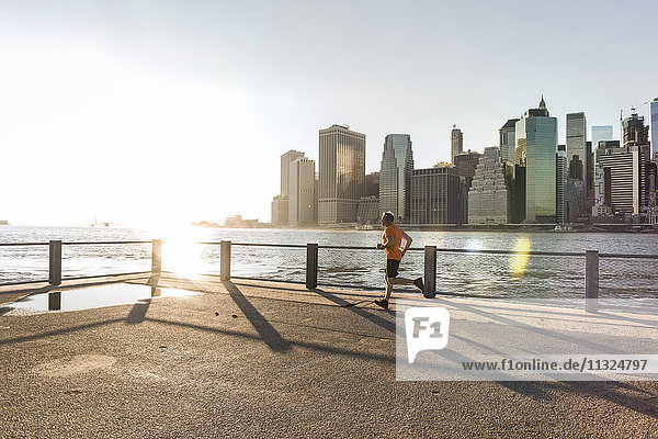 USA  Brooklyn  Mann joggen vor der Skyline von Manhattan am Abend