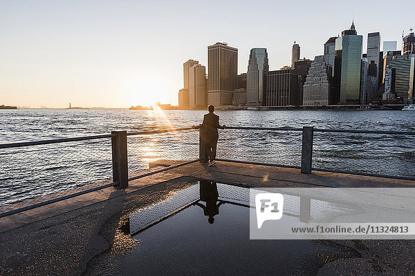 USA  Brooklyn  Rückansicht der Frau  die sich auf das Geländer stützt und den Sonnenuntergang betrachtet.