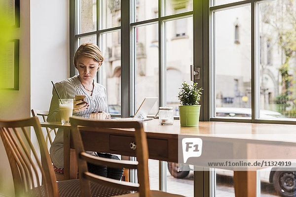 Junge Frau mit Handy und Tablette im Café