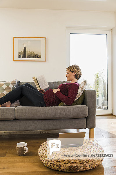 Pregnant woman on couch reading book