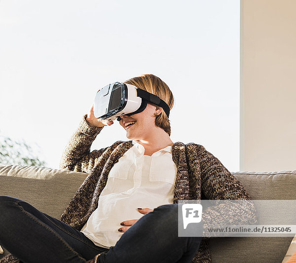 Schwangere auf der Couch mit VR-Brille