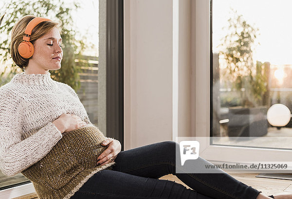 Eine schwangere Frau sitzt auf dem Boden und hört Musik.