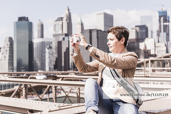 USA  New York City  Frau auf der Brooklyn Bridge macht Handyfoto