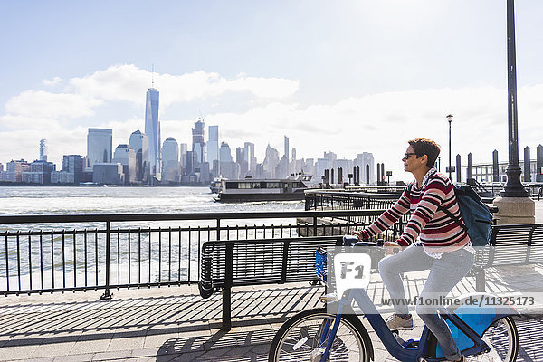 USA  Frau auf dem Fahrrad am New Jersey Waterfront mit Blick auf Manhattan