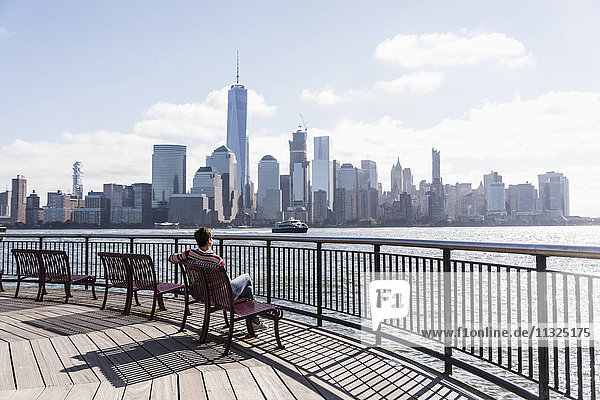 USA  Frau sitzt auf der Bank an der New Jersey Waterfront mit Blick auf Manhattan