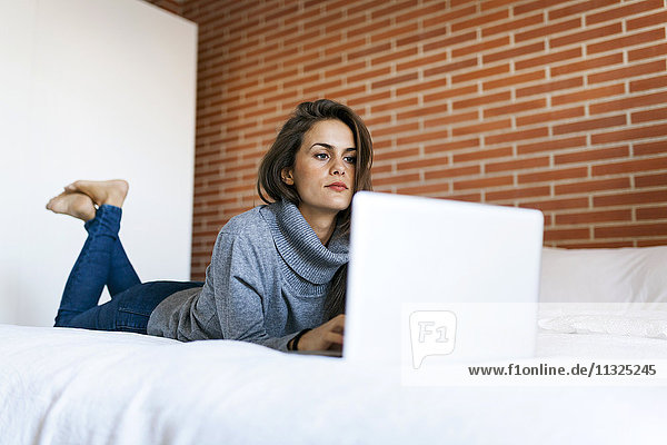 Junge Frau auf dem Bett liegend mit Laptop