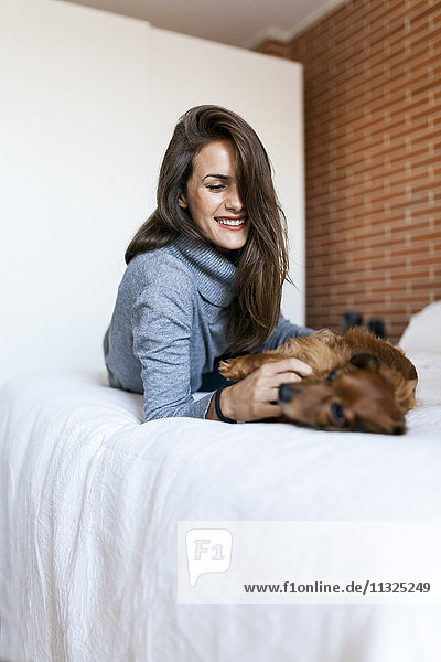 Glückliche junge Frau liegt im Bett und spielt mit ihrem Hund.