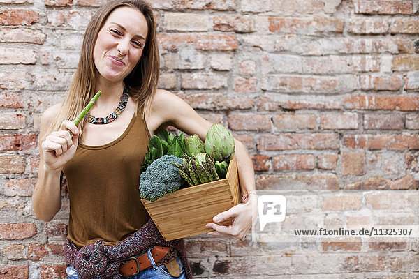 Lächelnde Frau hält Korb mit frischem Gemüse