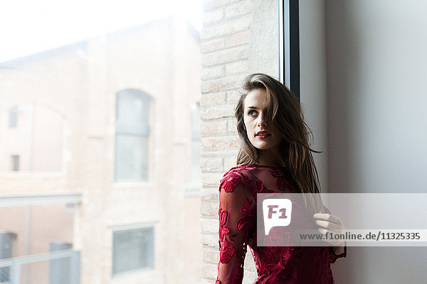 Schöne junge Frau im roten Kleid am Fenster