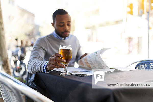 Junger Mann liest Zeitung und trinkt ein Bier im Straßencafé.