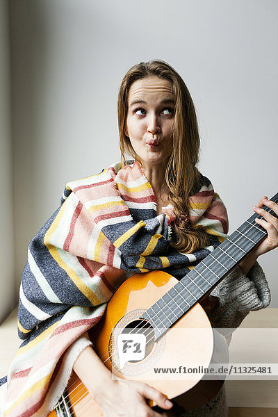Young woman with blanket and guitar pulling funny faces