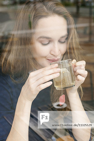 Lächelnde junge Frau trinkt eine Tasse Tee in einem Café.