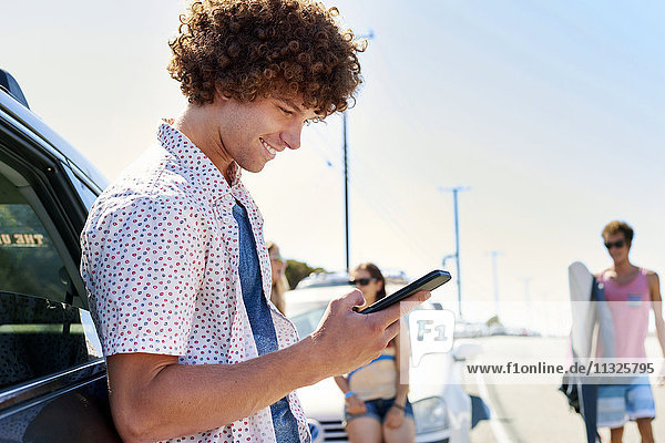 Smiling young man at a car checking his cell phone