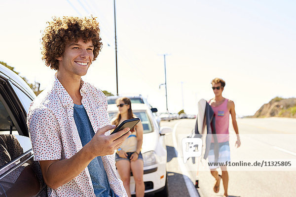 Lächelnder junger Mann an einem Auto mit Handy