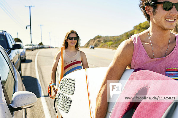 Smiling young couple carrying surfboards on coastal road