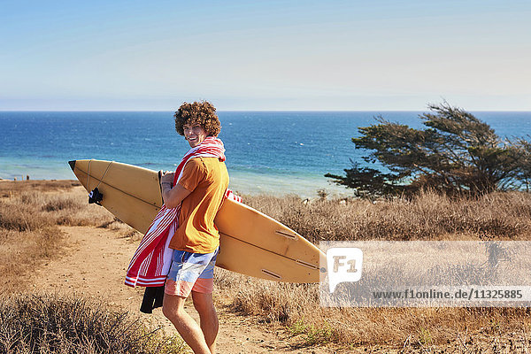 Junger Mann mit Surfbrett an der Küste