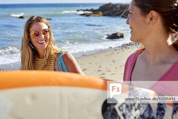 Two happy women carrying surfboards on the beach