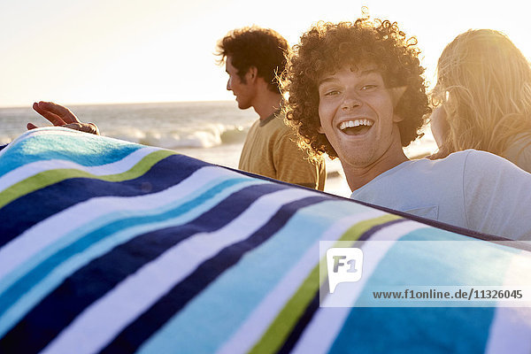 Glücklicher junger Mann mit Handtuch am Strand