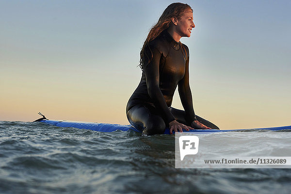 Frau sitzt auf dem Surfbrett im Meer bei Sonnenuntergang