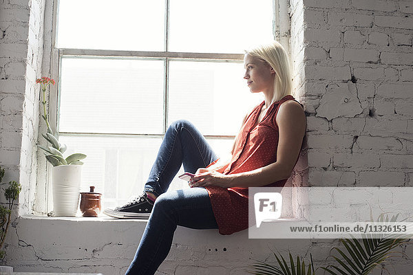 Junge Frau sitzt auf der Fensterbank in einem Loft