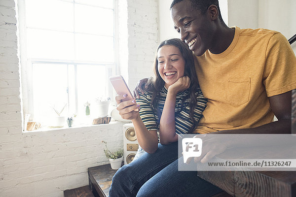 Happy young couple sitting on stairs in a loft sharing cell phone