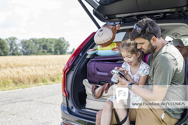 Vater und Tochter sitzen im offenen Kofferraum und schauen in die Kamera  wenn eine Autofahrt unterbrochen wird.