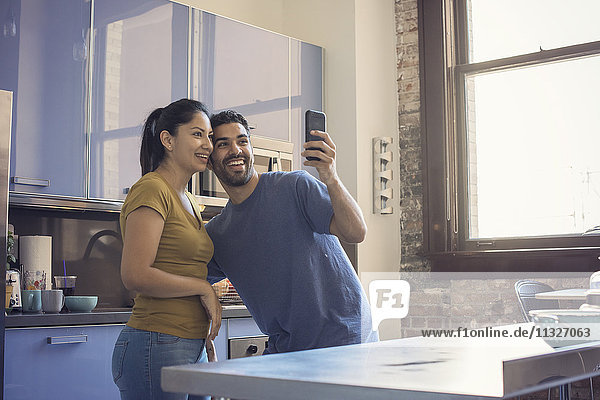 Young couple in kitchen taking selfie