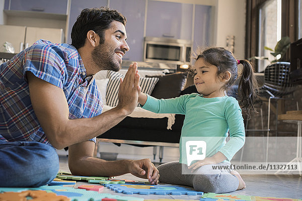 Vater und Tochter sitzen auf dem Boden und spielen mit dem Kinderpuzzle.