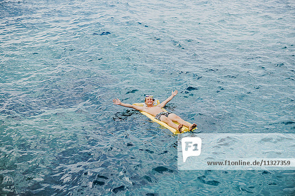 Fröhlicher junger Mann  der sich auf dem Luftbett im Meer entspannt.