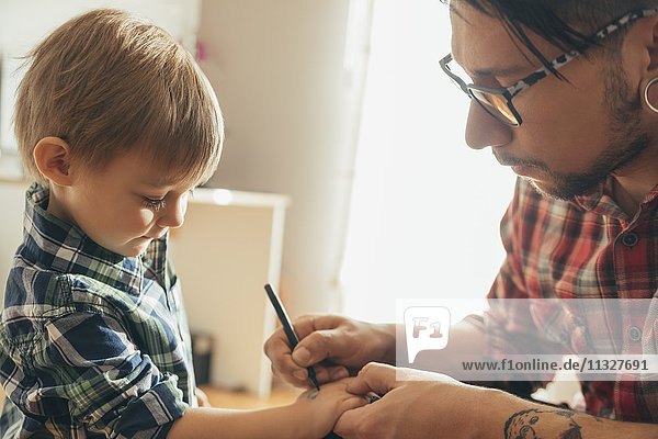 Vater malt Tattoo auf die Hand des Sohnes