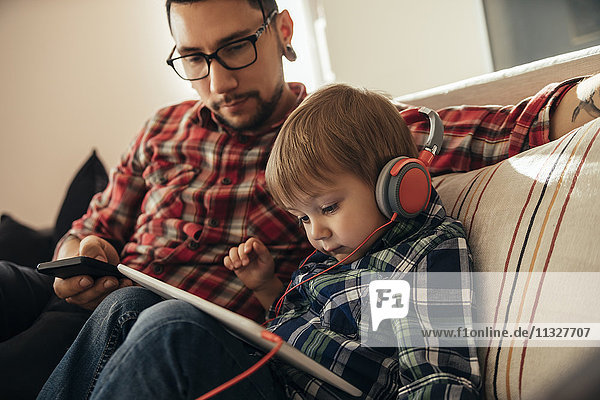 Vater und Sohn auf der Couch mit Tablett und Kopfhörer