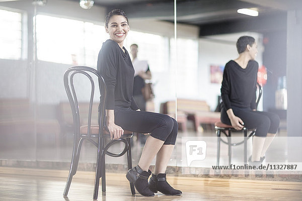 Porträt einer lächelnden Tänzerin  die auf einem Stuhl im Tanzstudio sitzt.
