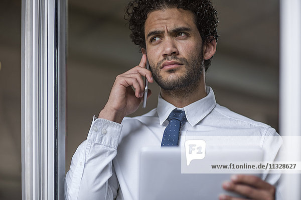 Businessman with cell phone and tablet looking out of window
