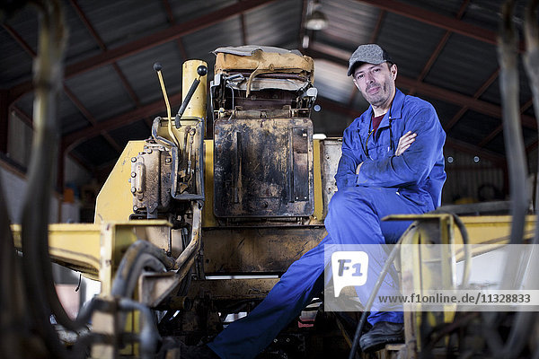 Mann im blauen Overall sitzend auf der Maschine in der Werkstatt