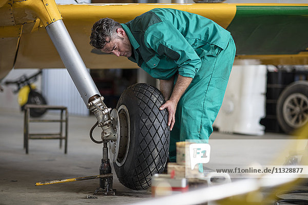Mechanic in hangar repairing light aircraft  fixing tire