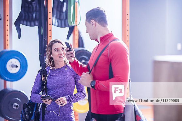 Junger Mann und Frau mit Handys und Ohrhörern im Fitnessstudio