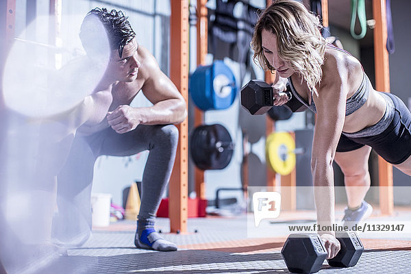 Fitnesstrainerin mit Frau beim Hantelpressen im Fitnessstudio