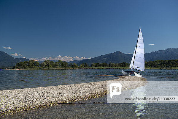 Outrigger sailboat moored on lakeshore against blue sky  Lake Chiemsee  Bavaria  Germany