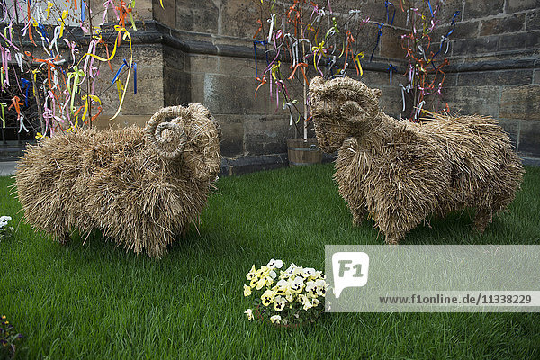 Sheep made from hay on grass against stone wall