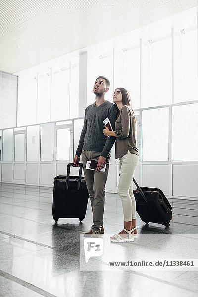 Volle Länge des jungen Paares mit Gepäck und Bordkarten am Flughafen