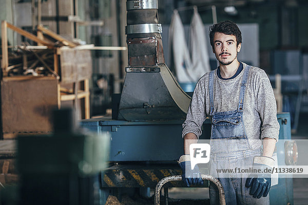 Portrait of carpenter standing by machinery at workshop