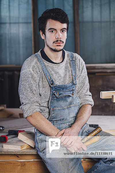 Porträt eines jungen Arbeiters  der mit Handwerkzeugen auf der Bank sitzt.