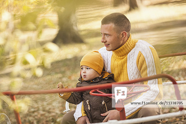 Thoughtful man sitting with baby boy on carousel at park during autumn