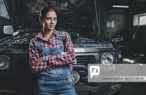 Portrait of confident female mechanic with arms crossed leaning on car at workshop