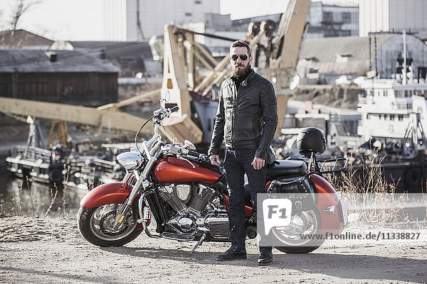 Vollständiges Porträt eines Motorradfahrers  der sich gegen die industrielle Umgebung stellt.