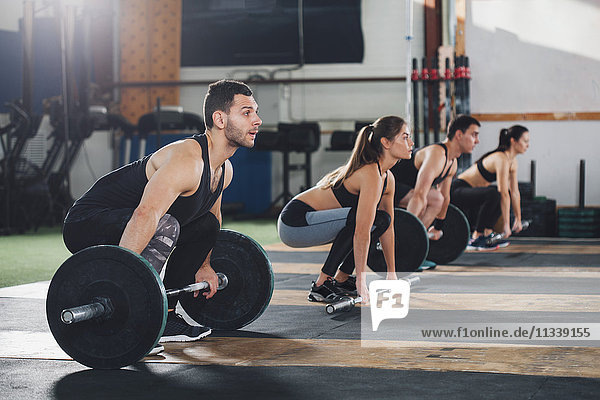 Dedicated male and female athletes lifting barbells at gym