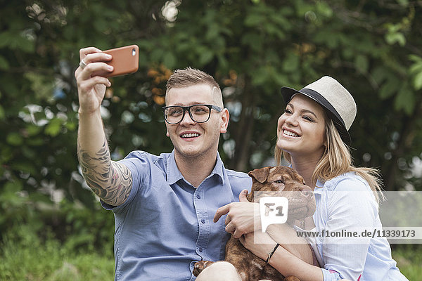 A couple with their Shar-pei/Staffordshire Terrier dog at the park taking a selfie
