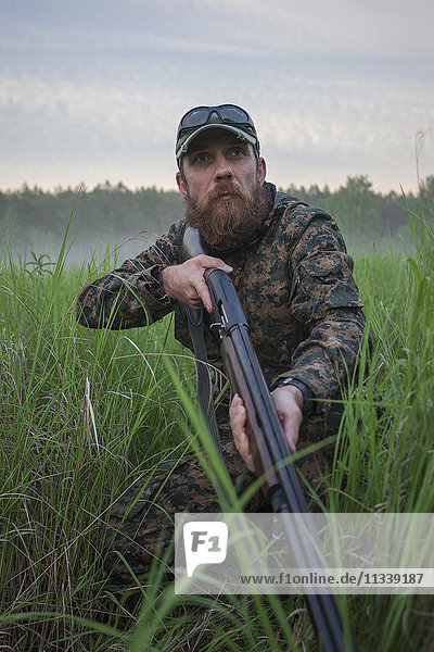 Jäger hält Gewehr  während er auf das Feld schaut.