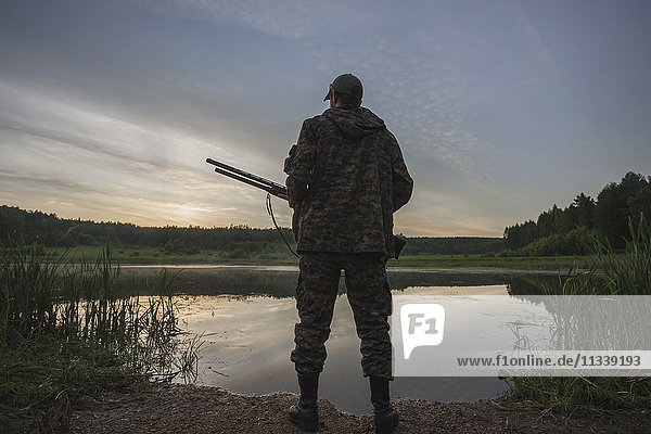 Rückansicht des Jägers am Seeufer bei Sonnenuntergang