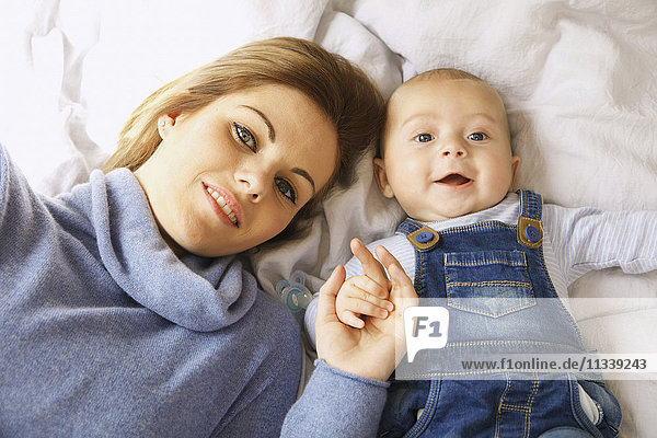 Directly above shot of happy mother lying with cute baby boy on bed
